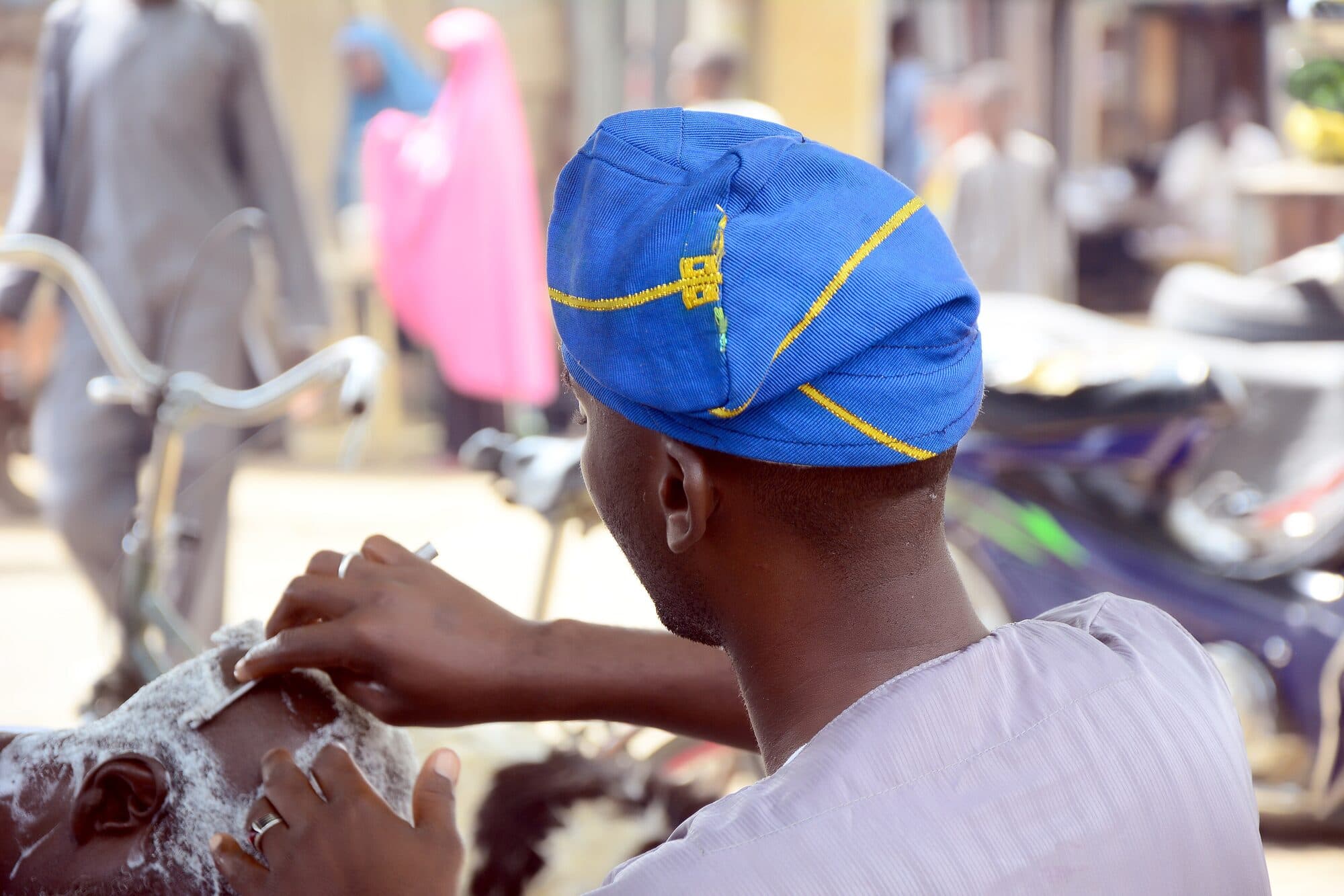 A barber at work in the open air, customer under a cape