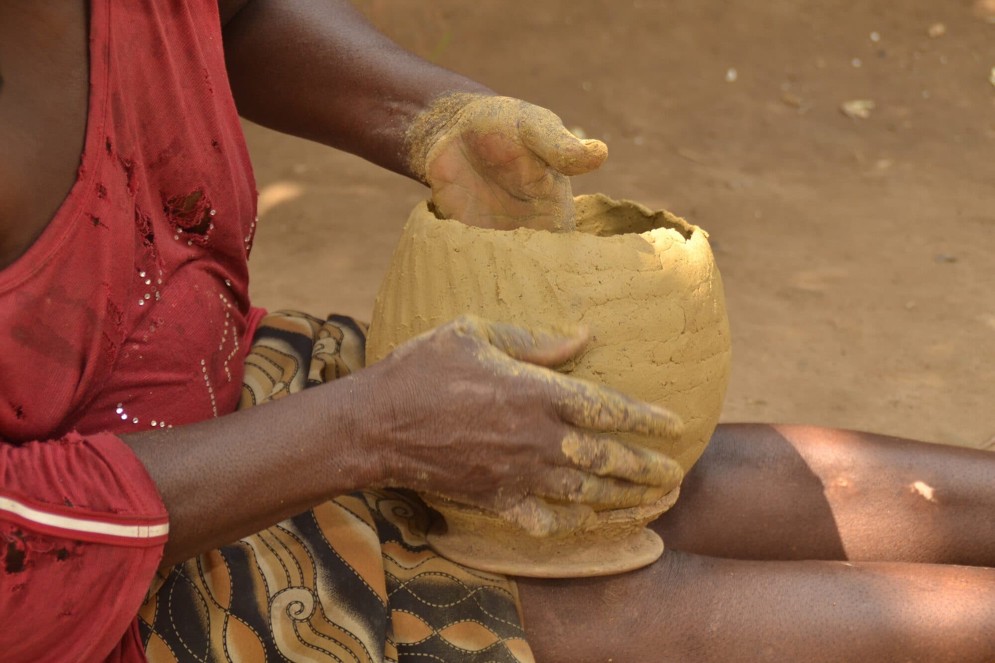 Hands shaping the wall of a large clay pot