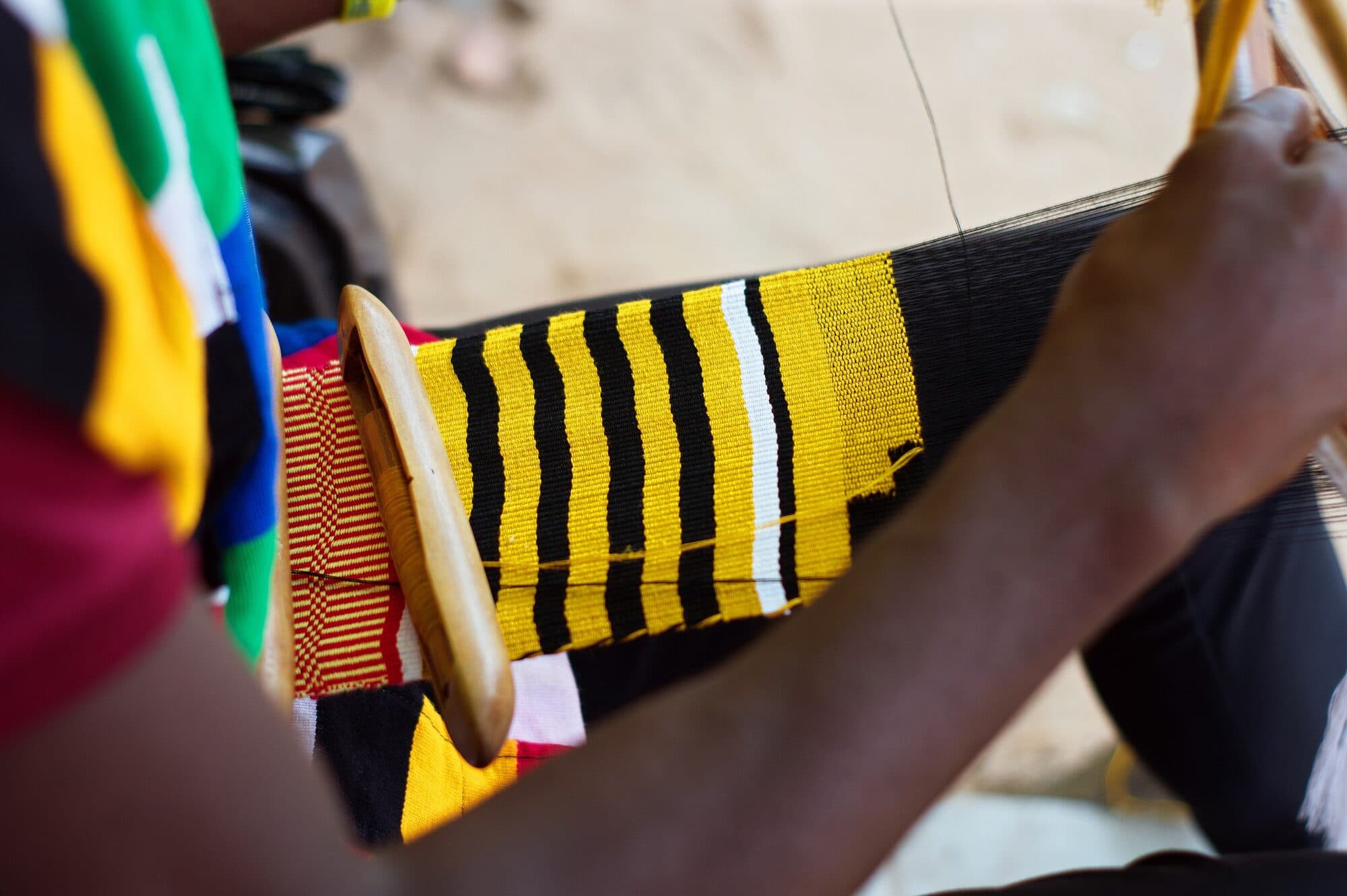 Hands beating the weft on a narrow kente loom