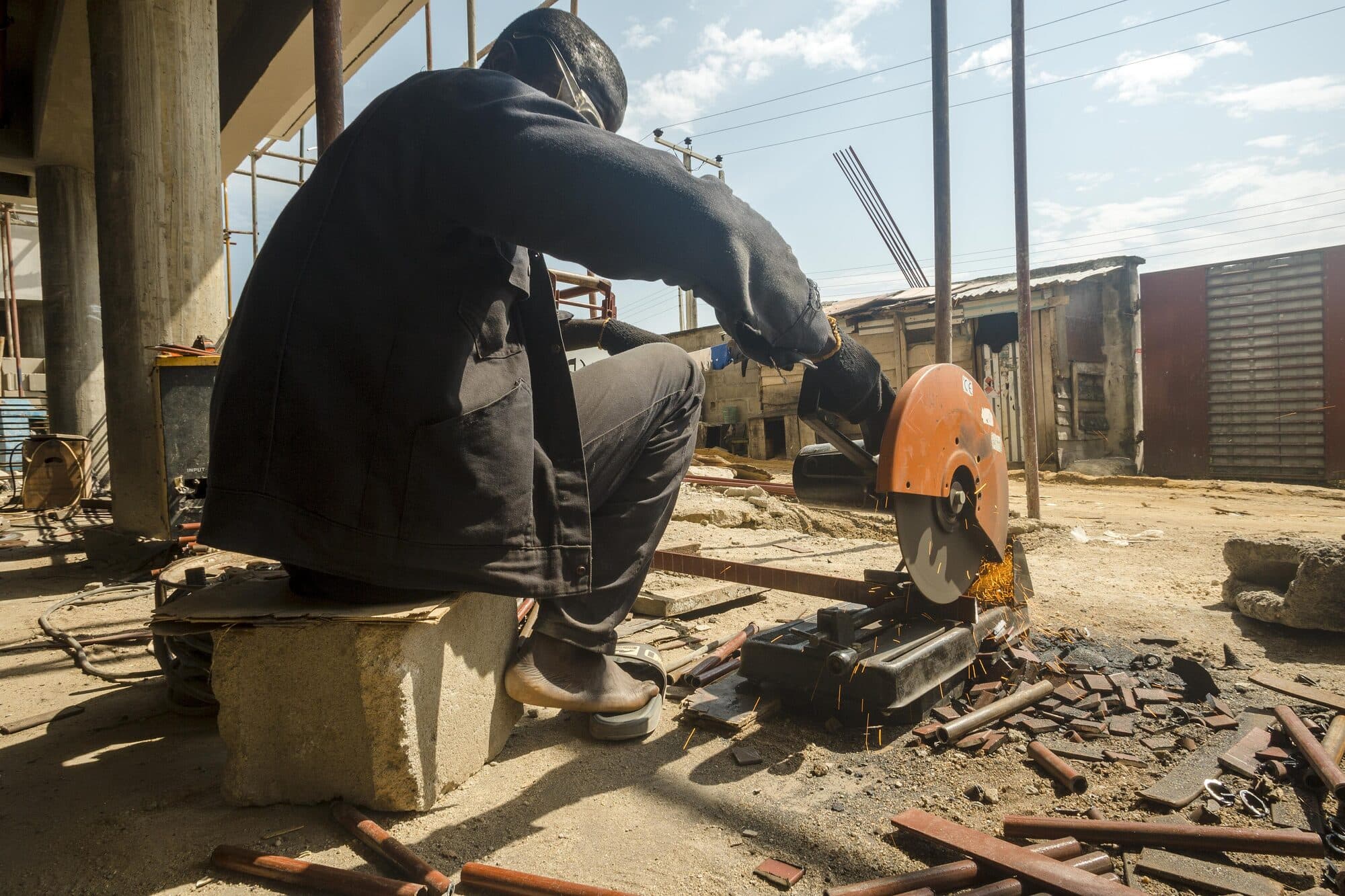 A man working scrap metal at a roadside fabrication yard