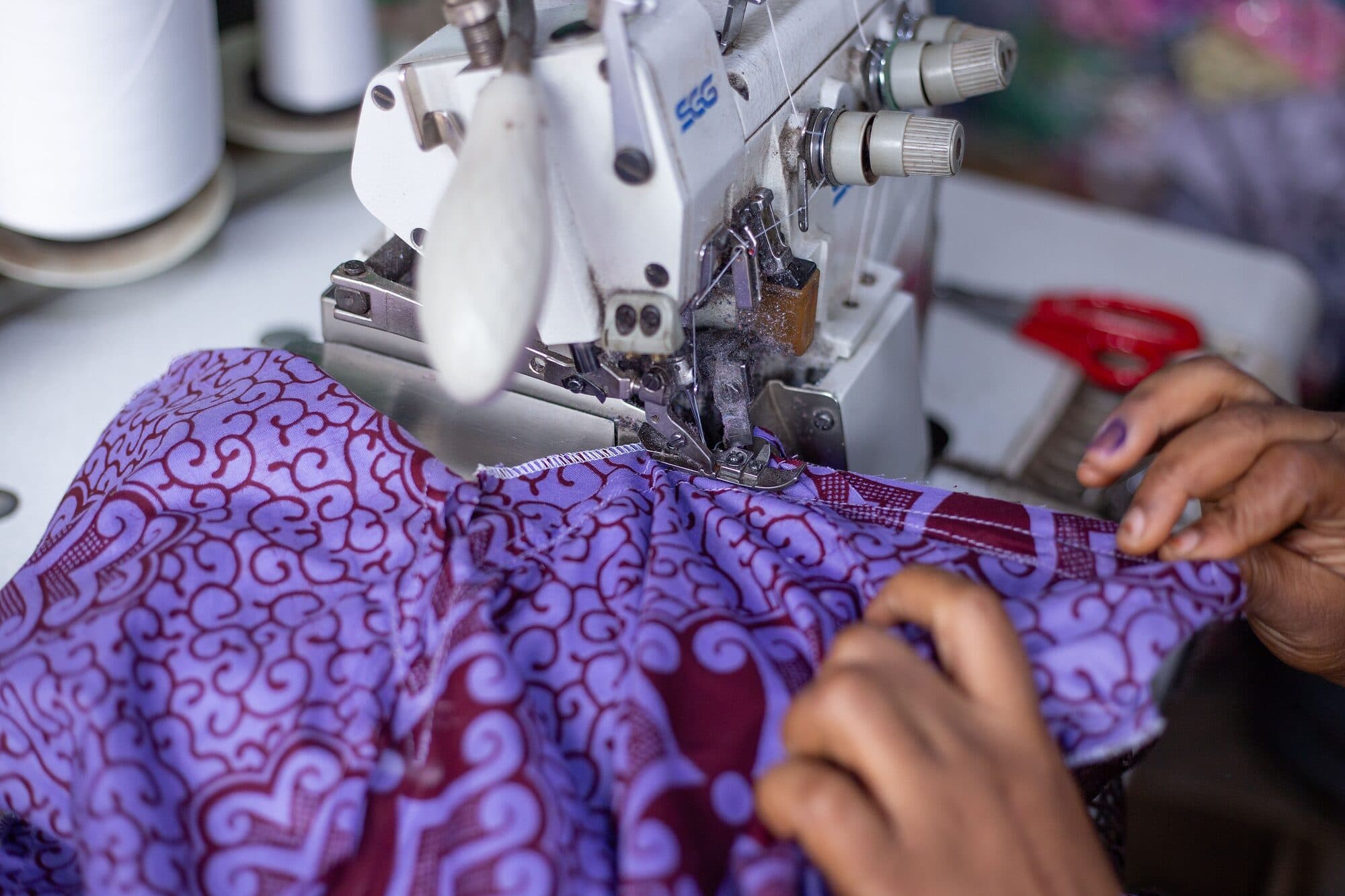 Hands guiding printed cloth under a sewing machine needle